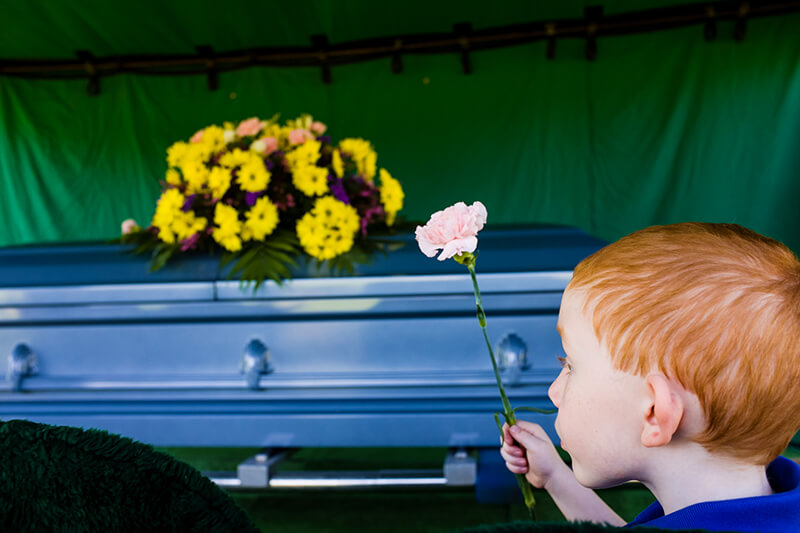 child at funeral offering flower to casket